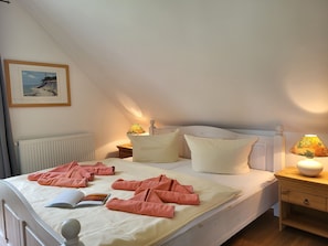 A neatly made bed with pink towels, a framed picture on the wall, and a lamp on the nightstand.
