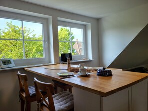 A dining area with a wooden table, two chairs, a laptop, a teapot, and a cup on the windowsill. - Vacation apartment Frida, Germany (Ahrenshoop)