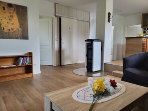 A living room with a wooden coffee table, a bookshelf, a painting, a fireplace, and a kitchen area.