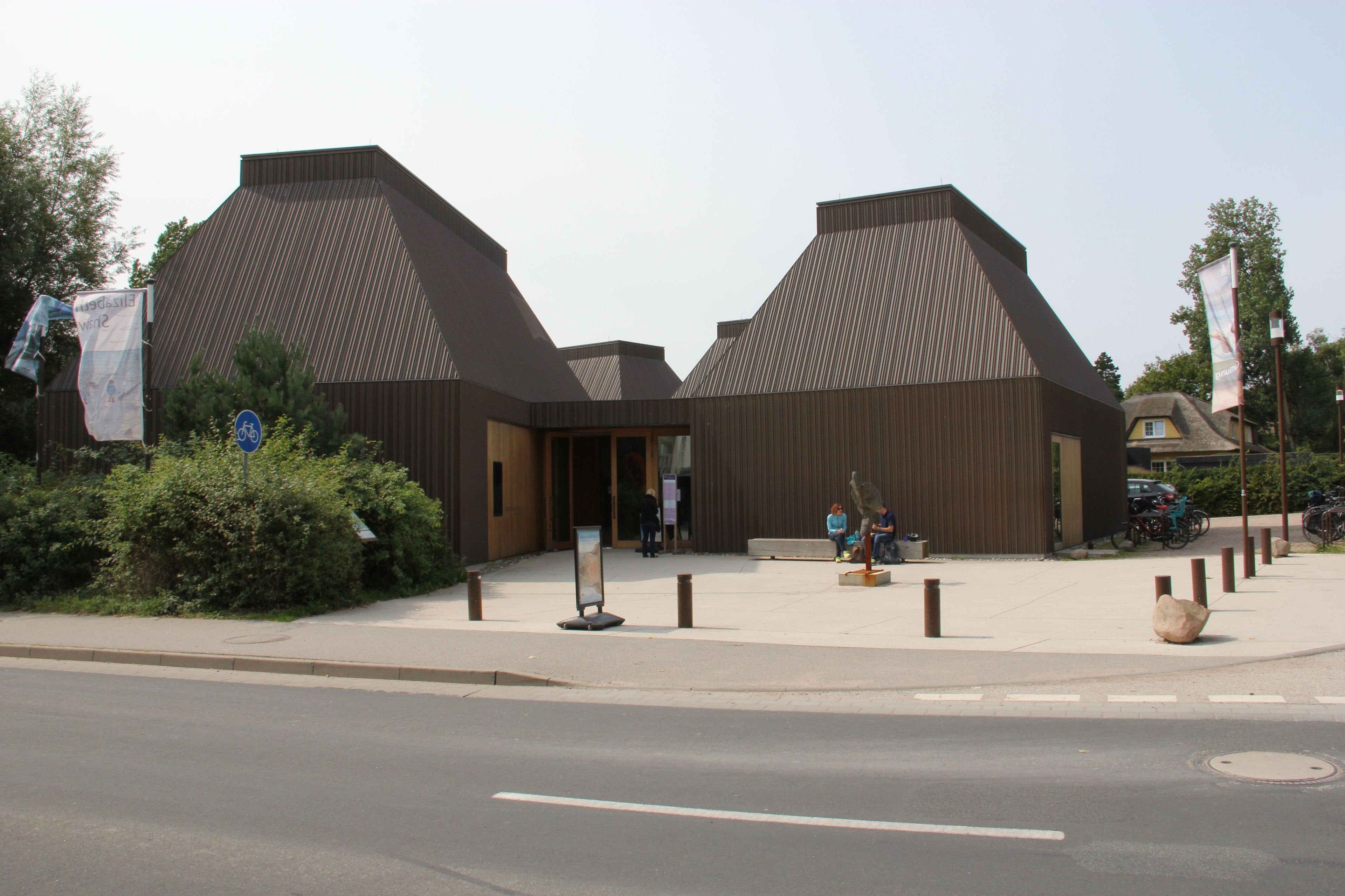 A modern building with a unique architectural design, featuring a large entrance and a small seating area outside.