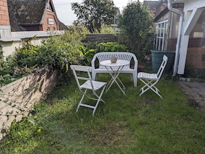 A small outdoor seating area with a table and two chairs, surrounded by greenery and a brick wall. - Vacation apartment Frida, Germany (Ahrenshoop)