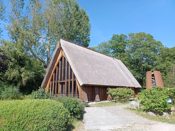 A rustic building with a steeply pitched roof, wooden framing, and a thatched roof.