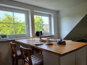 A dining area with a wooden table, two chairs, a laptop, a teapot, and a cup on the windowsill. - Vacation apartment Frida, Germany (Ahrenshoop)