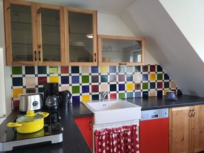 A kitchen with wooden cabinets, a colorful tiled backsplash, a yellow pot on the stove, a coffee maker, and a sink. - Vacation apartment Frida, Germany (Ahrenshoop)