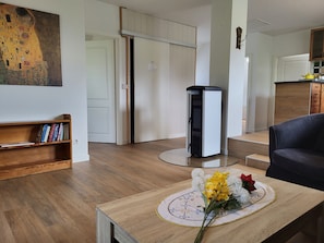 A living room with a wooden coffee table, a bookshelf, a painting, a fireplace, and a kitchen area.