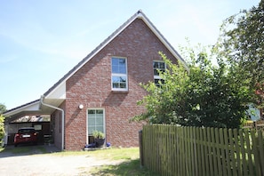A red brick house with a garage, a wooden fence, and a potted plant. - Vacation apartment Frida, Germany (Ahrenshoop)