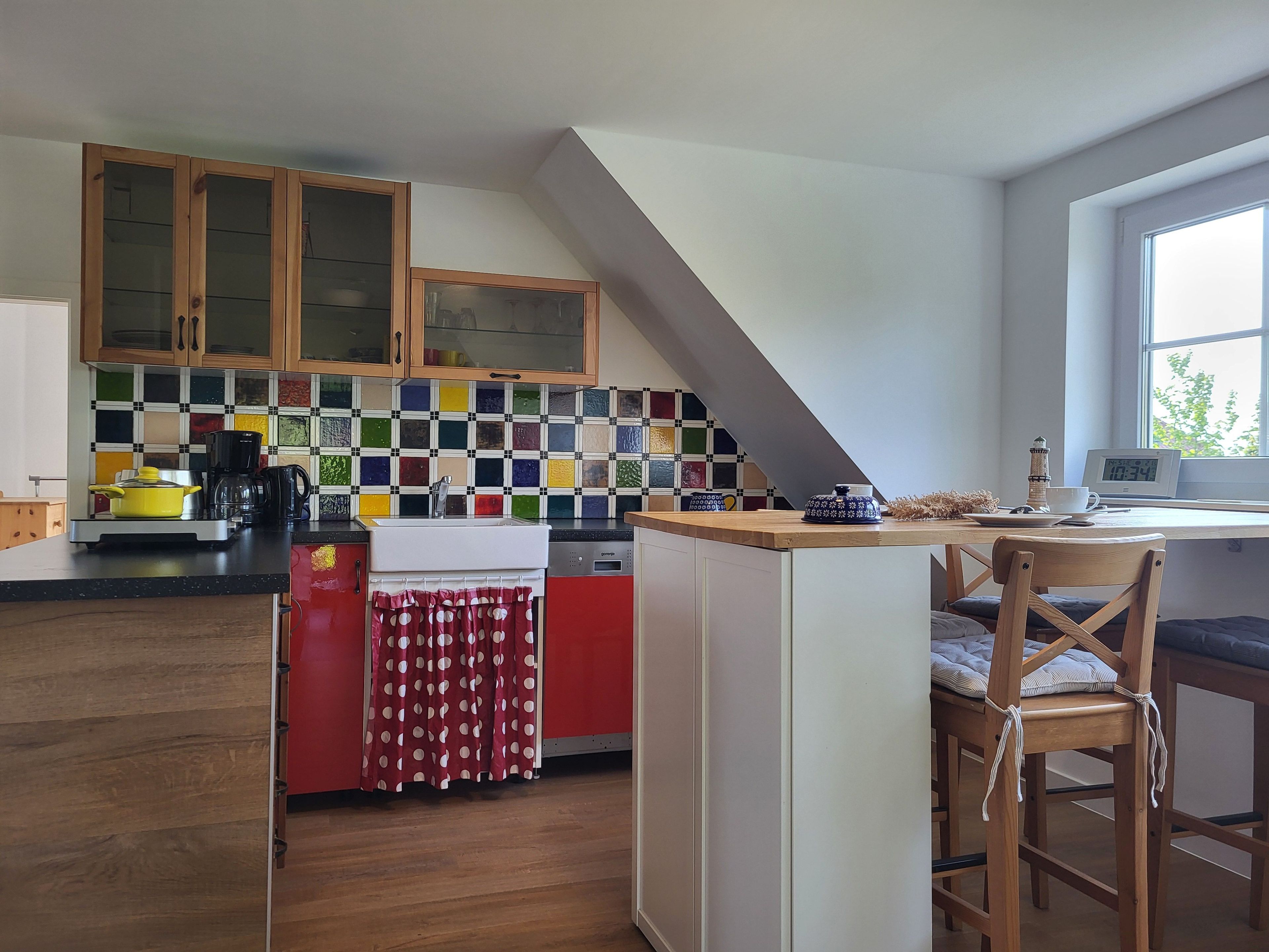 Une cuisine avec des meubles en bois, un crédence aux couleurs vives, un coin repas avec une table et des chaises, et une fenêtre offrant une belle vue.