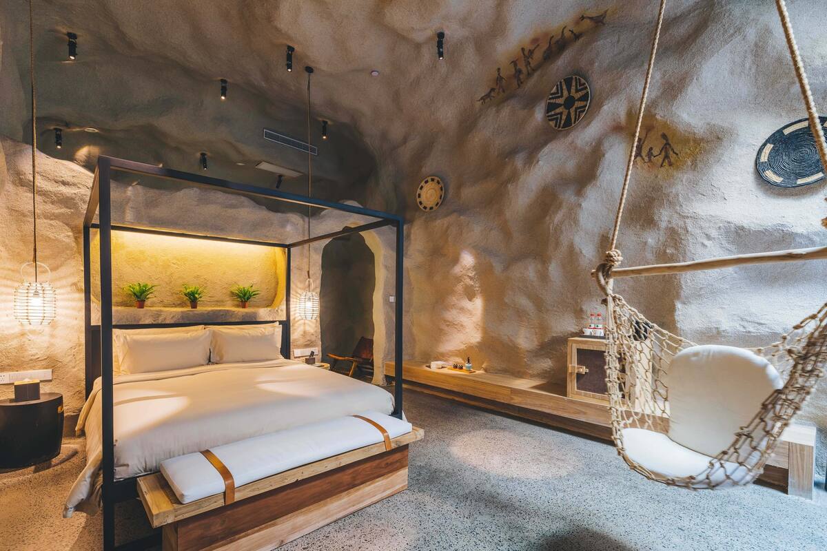Een slaapkamer met een hemelbed, een hangstoel en een stenen muur.