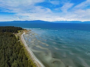 An aerial view of a coastal area with a forested shoreline, clear waters, and distant mountains.