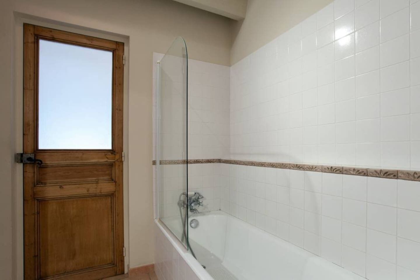 Ein Badezimmer mit Holztür, Duschkabine aus Glas und weiß gefliesten Wänden.