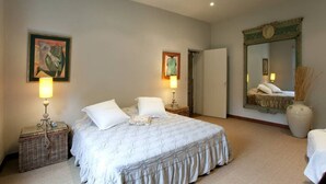 A bedroom with a large bed, two bedside tables with lamps, a mirror, and artwork on the walls.