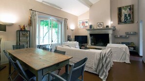 A cozy living room with a wooden table, two covered sofas, a fireplace, and a large window with curtains.