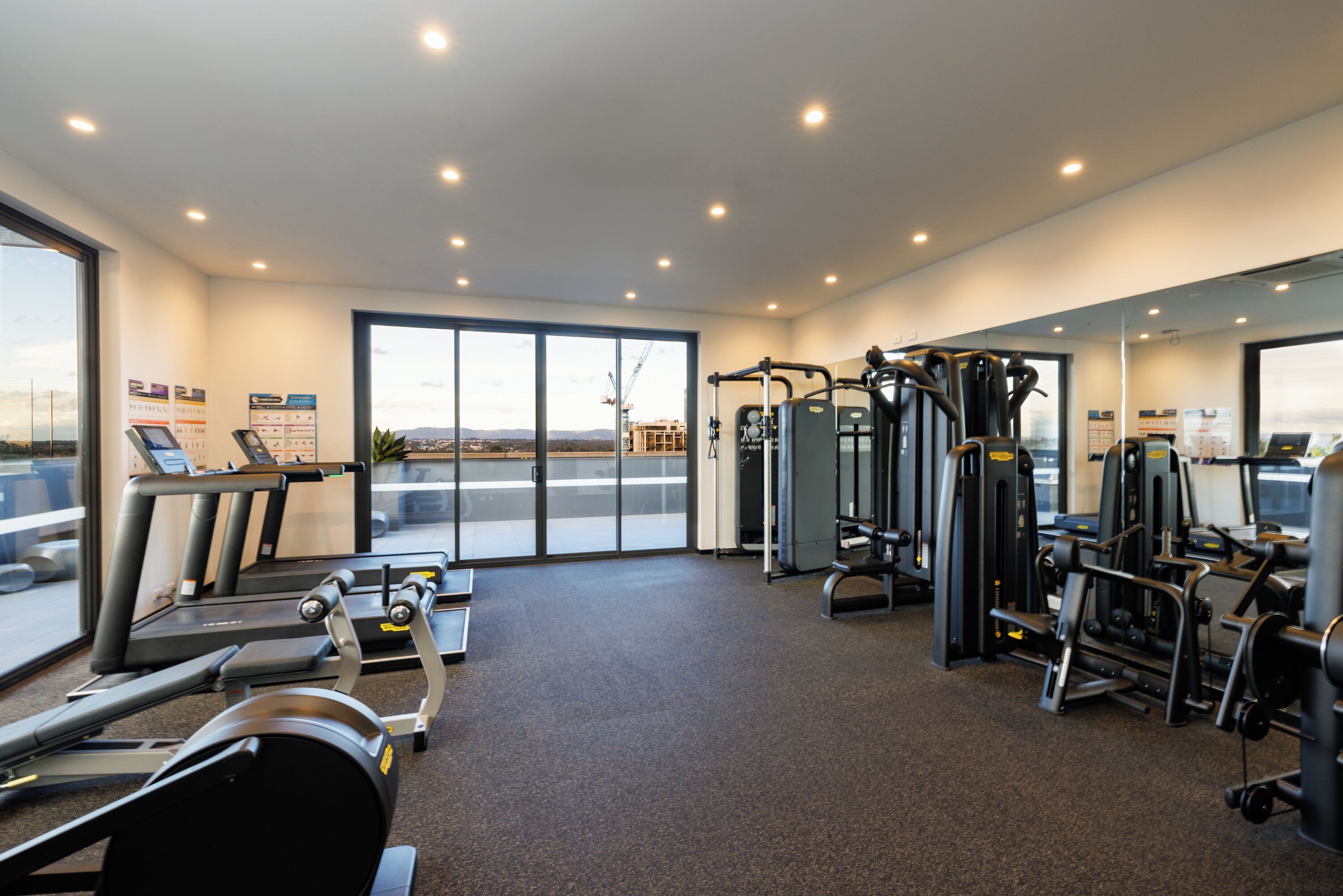 A gym with treadmills, weight machines, and a large window with a view of a cityscape.