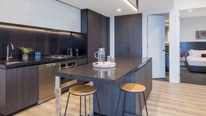 Une cuisine moderne avec des meubles de couleur sombre, un îlot central doté de tabourets et un lave-vaisselle encastré.