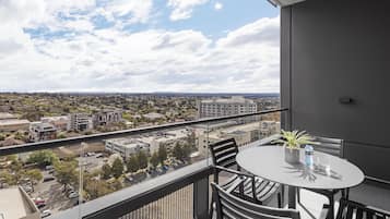 A balcony with a table and chairs, overlooking a cityscape with buildings and a clear sky.