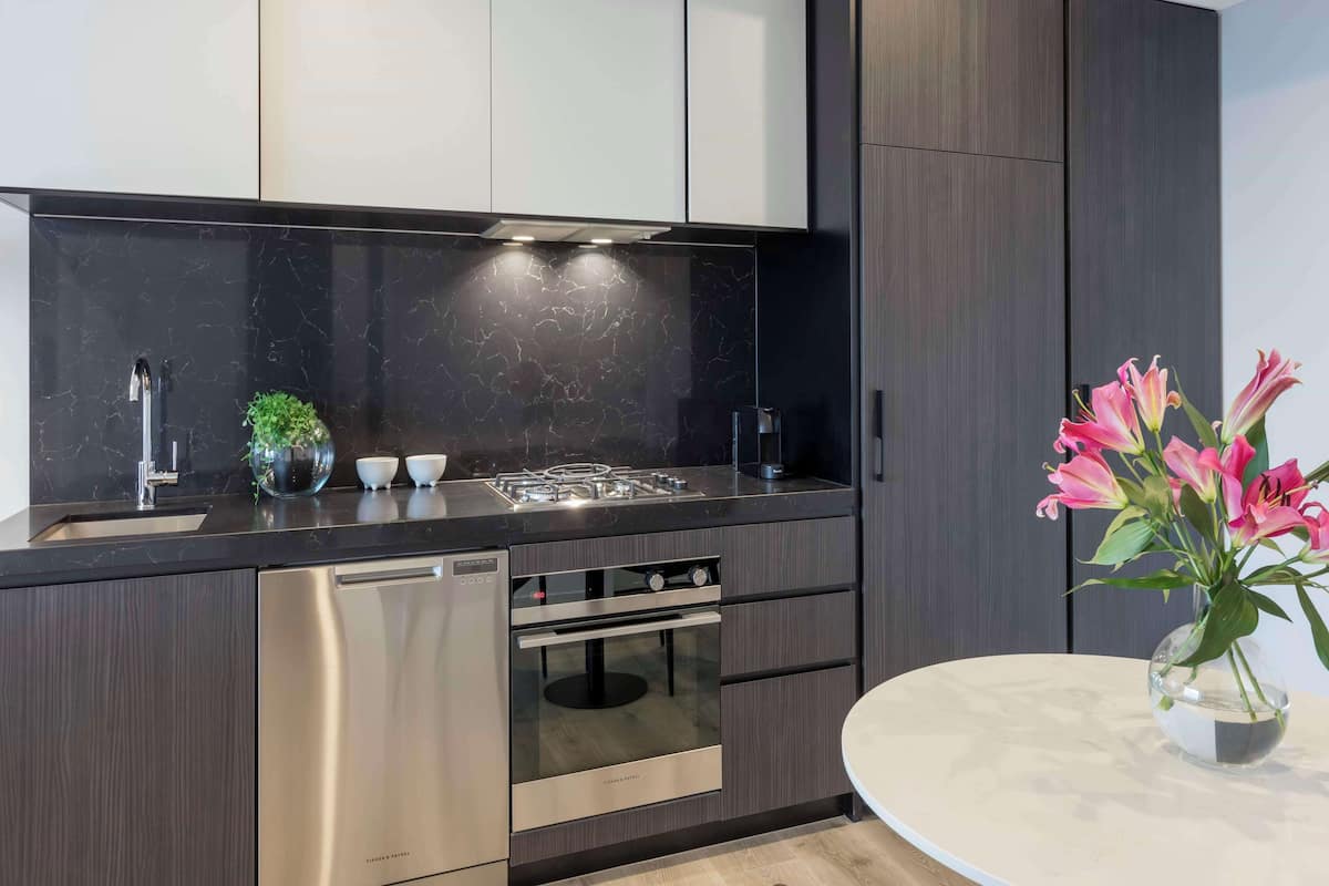 A modern kitchen with dark cabinetry, stainless steel appliances, and a marble countertop.
