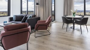A modern living room with a sofa, chairs, a dining table, and large windows offering a city view. - Avani Melbourne Box Hill Residences (Box Hill)