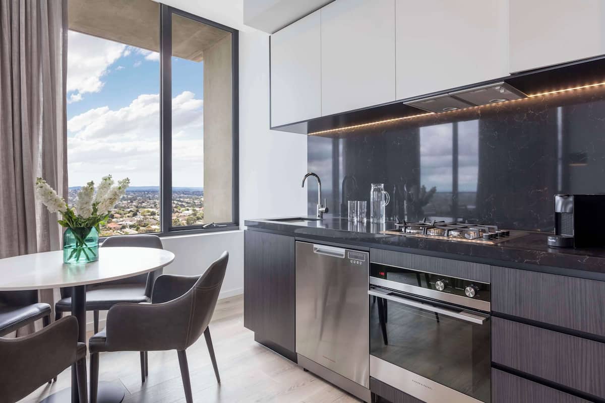 A modern kitchen with a built-in oven, dishwasher, and a large window offering a city view.