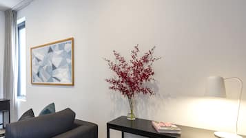 A modern room with a grey sofa, a black desk, a vase with red flowers, a framed geometric artwork, and a white lamp.