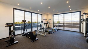 A modern gym with treadmills, an elliptical, and a weight machine, featuring large windows and a view of the city. - Avani Melbourne Box Hill Residences (Box Hill)
