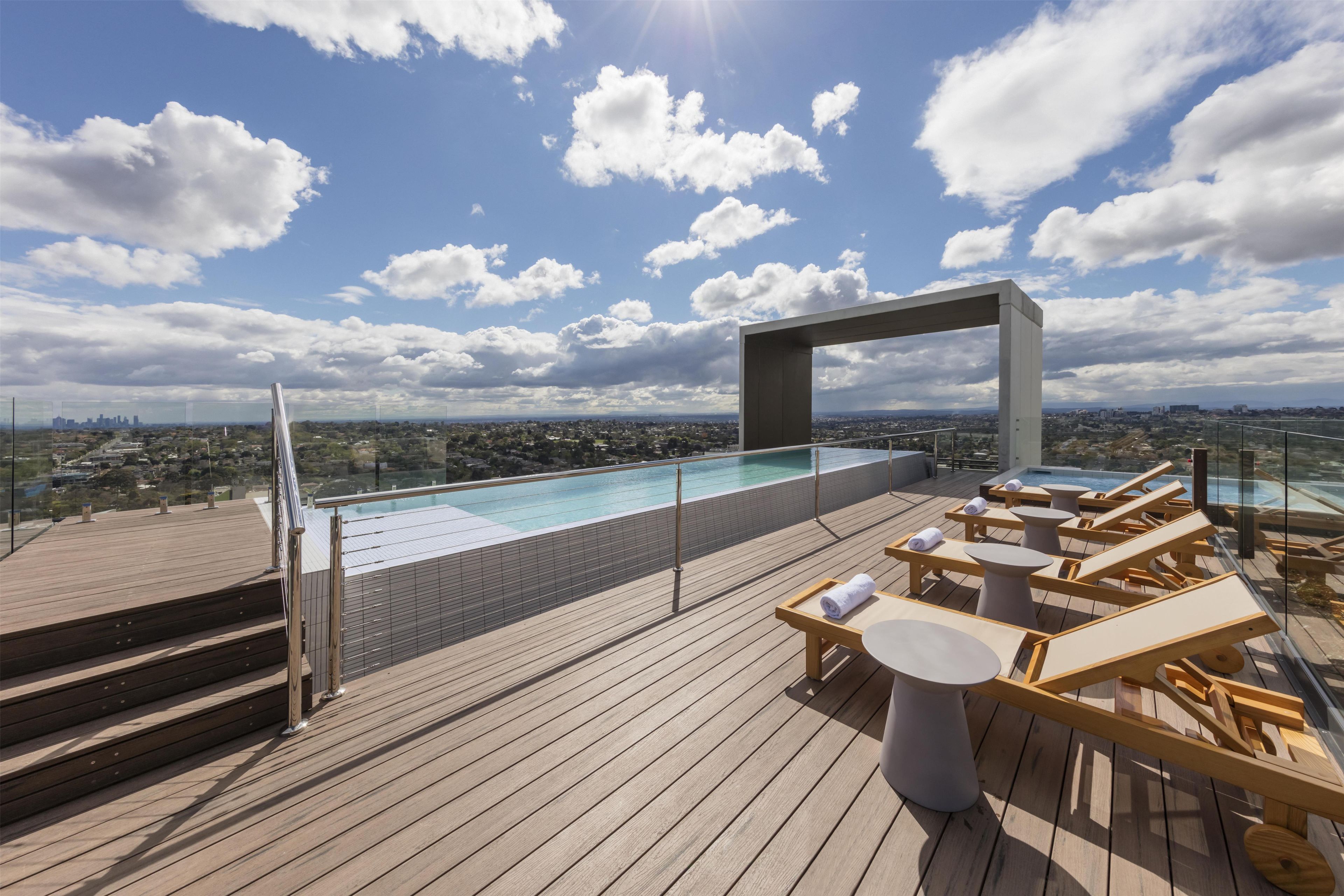 Área de piscina en la azotea con sillas de descanso y vistas a la ciudad.
