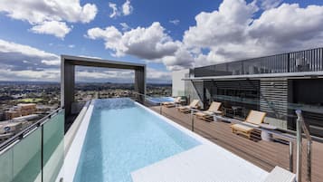 A rooftop infinity pool with a clear view of the cityscape, lounge chairs, and a modern building structure.