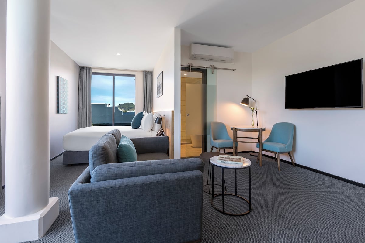 A hotel room with a bed, a sofa, a TV, and a desk with chairs.