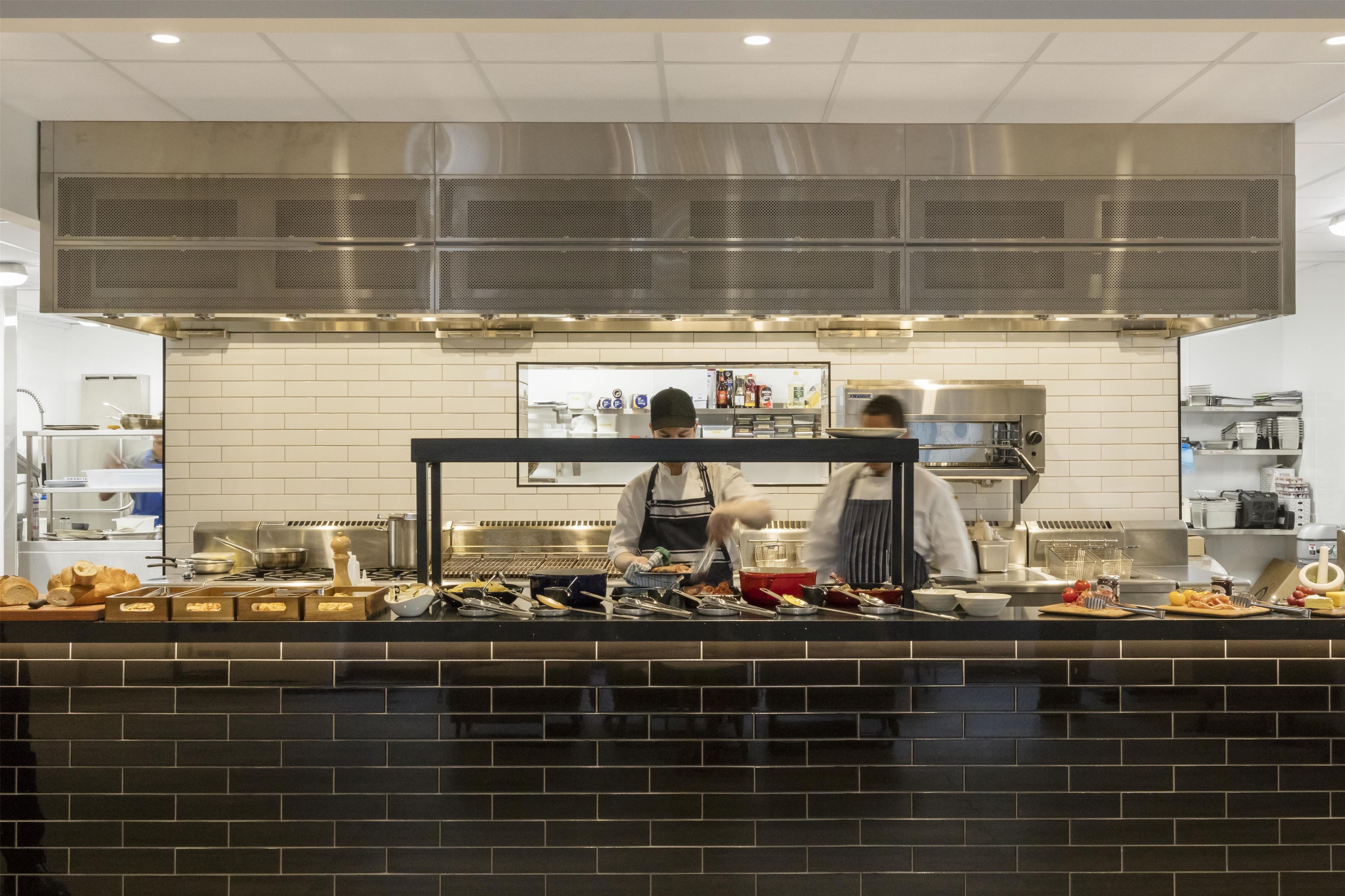 A commercial kitchen with stainless steel appliances, a tiled backsplash, and a counter with various food items and utensils.