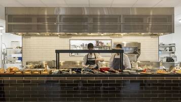 Cocina comercial con electrodomésticos de acero inoxidable, salpicadero de azulejos y una encimera con diversos alimentos y utensilios.