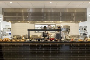 Cocina comercial con electrodomésticos de acero inoxidable, salpicadero de azulejos y una encimera con diversos alimentos y utensilios.