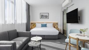 Quarto de hotel com cama, sofá, mesinha com copos, televisão e quadro na parede.
