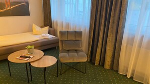 A hotel room with a sofa, a chair, a small table, and a view of a bridge.