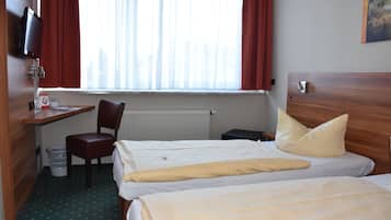 Et hotelværelse med to senge, et skrivebord med stol, et fjernsyn og et vindue med gardiner.