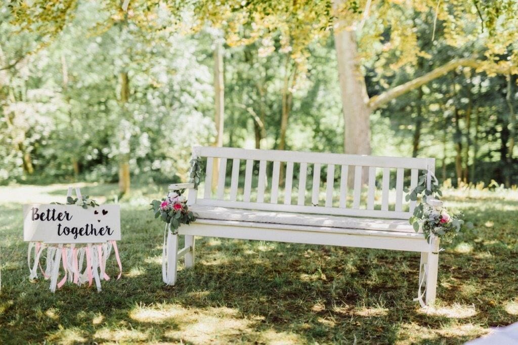 A white bench with a sign that reads "Better together" and a small bouquet of flowers.