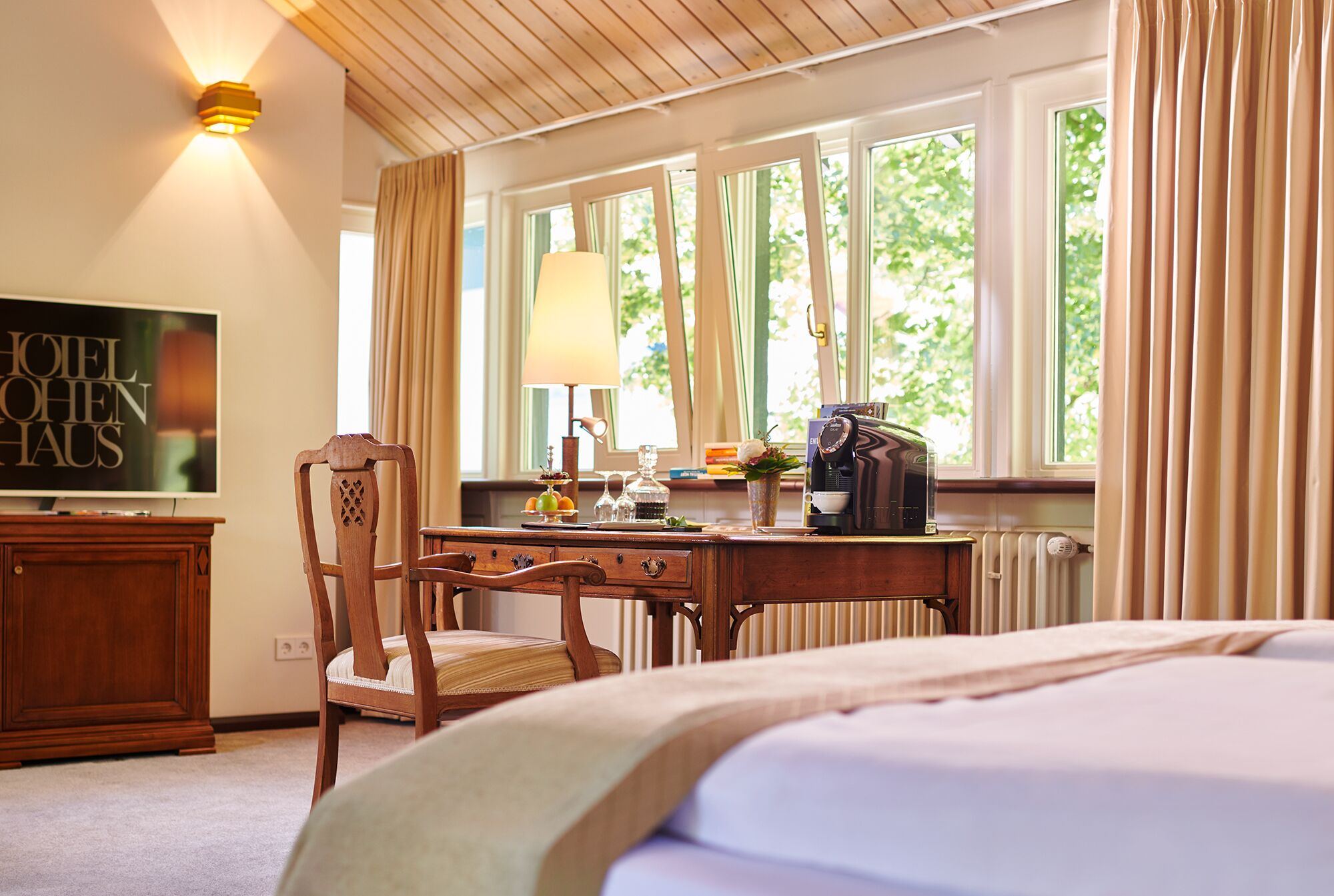 A hotel room with a bed, a wooden desk, a chair, a television, and a window with curtains.