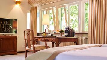 A hotel room with a bed, a wooden desk, a chair, a television, and a window with curtains.