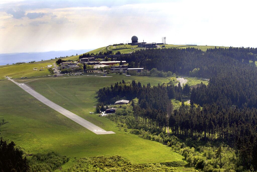 A rural airport with a runway, buildings, and a forested hill.