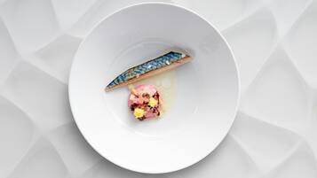 Un plato blanco con un trozo de pescado y una porción pequeña de comida rosa y amarilla.