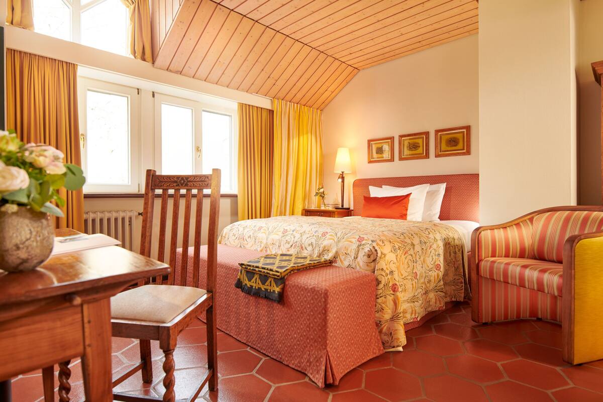Una habitación de hotel con cama, una silla, una mesa y un armario de madera.