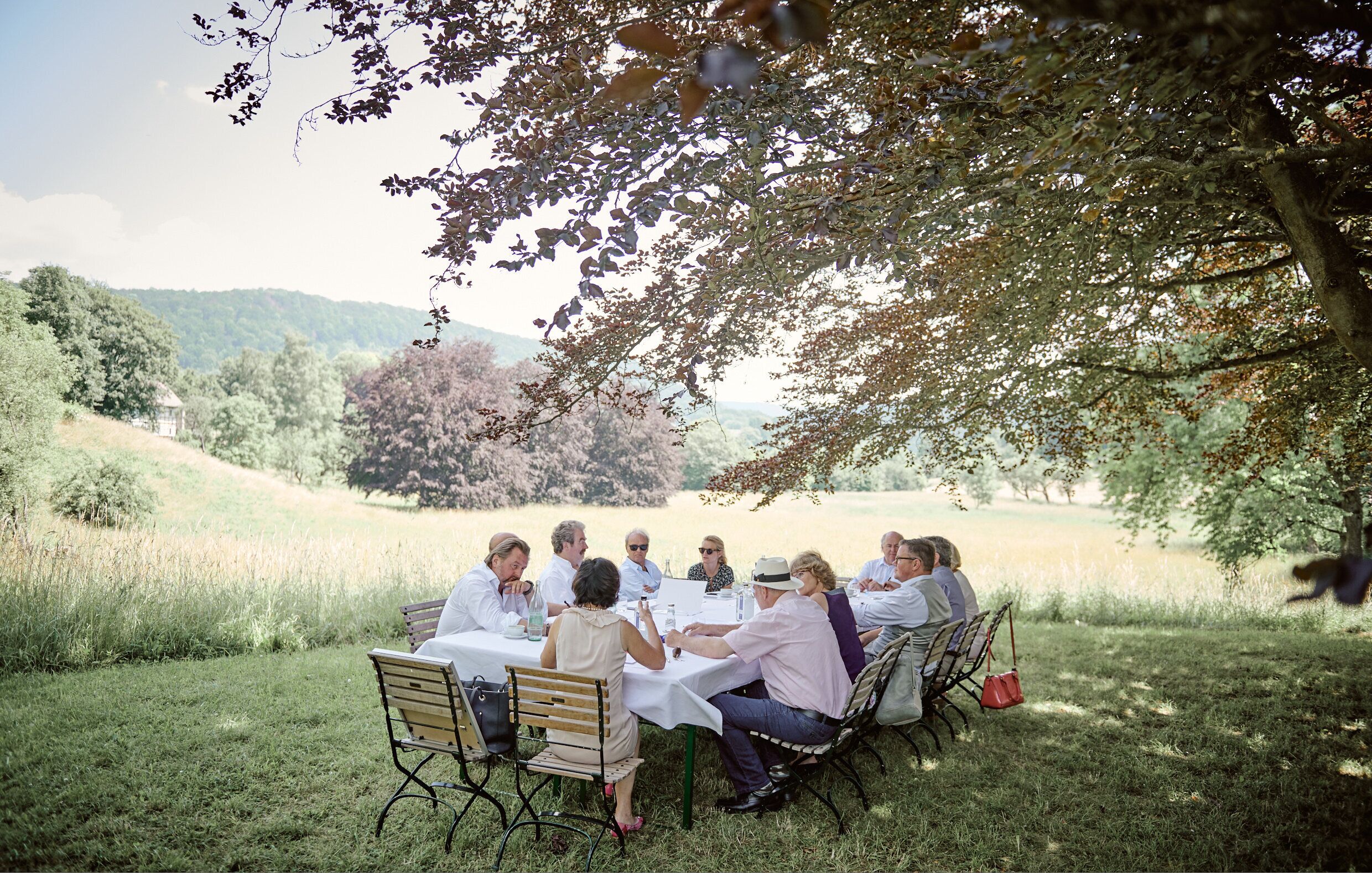 Un gruppo di persone sedute a un tavolo all'aperto, circondate da vegetazione e alberi.