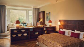 A hotel room with a bed, a desk with bowls, a chair, a lamp, and a painting on the wall.