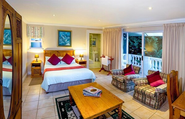 A hotel room with a large bed, two bedside tables, a wooden coffee table, a sofa set, and a view of the outdoors.