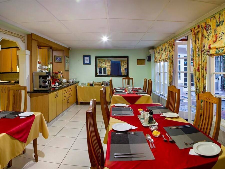 A dining area with tables set for four, a kitchen in the background, and a view through the window.