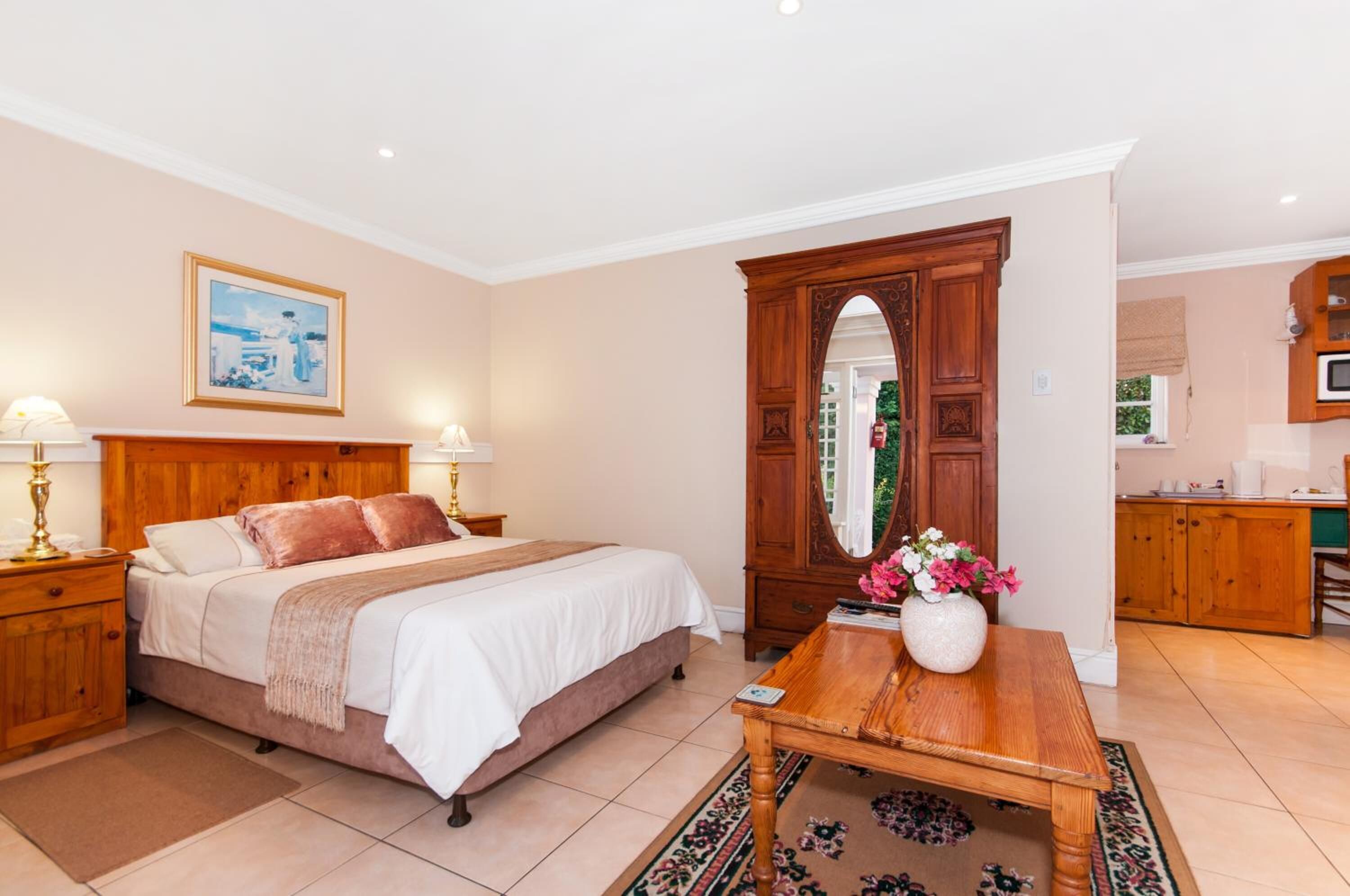 Un dormitorio con una cama de madera, mesitas de noche, un espejo y una pequeña mesa con un jarrón de flores.