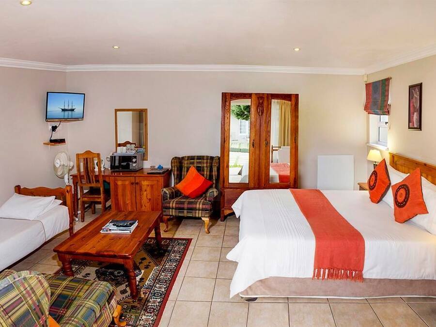 A hotel room with two single beds, a wooden coffee table, a sofa, a TV, and a desk with a chair.
