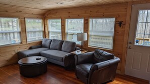 Un interior de cabaña acogedor con un sofá seccional, un sillón de cuero y una mesa de centro redonda.