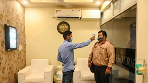A room with two white sofas, a clock on the wall, and an air conditioning unit. - Ganga Darshanam Guest House (Varanasi)