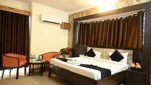 A hotel room with a large bed, two chairs, a small table with water bottles, a plant, and a nightstand with a lamp. - Ganga Darshanam Guest House (Varanasi)