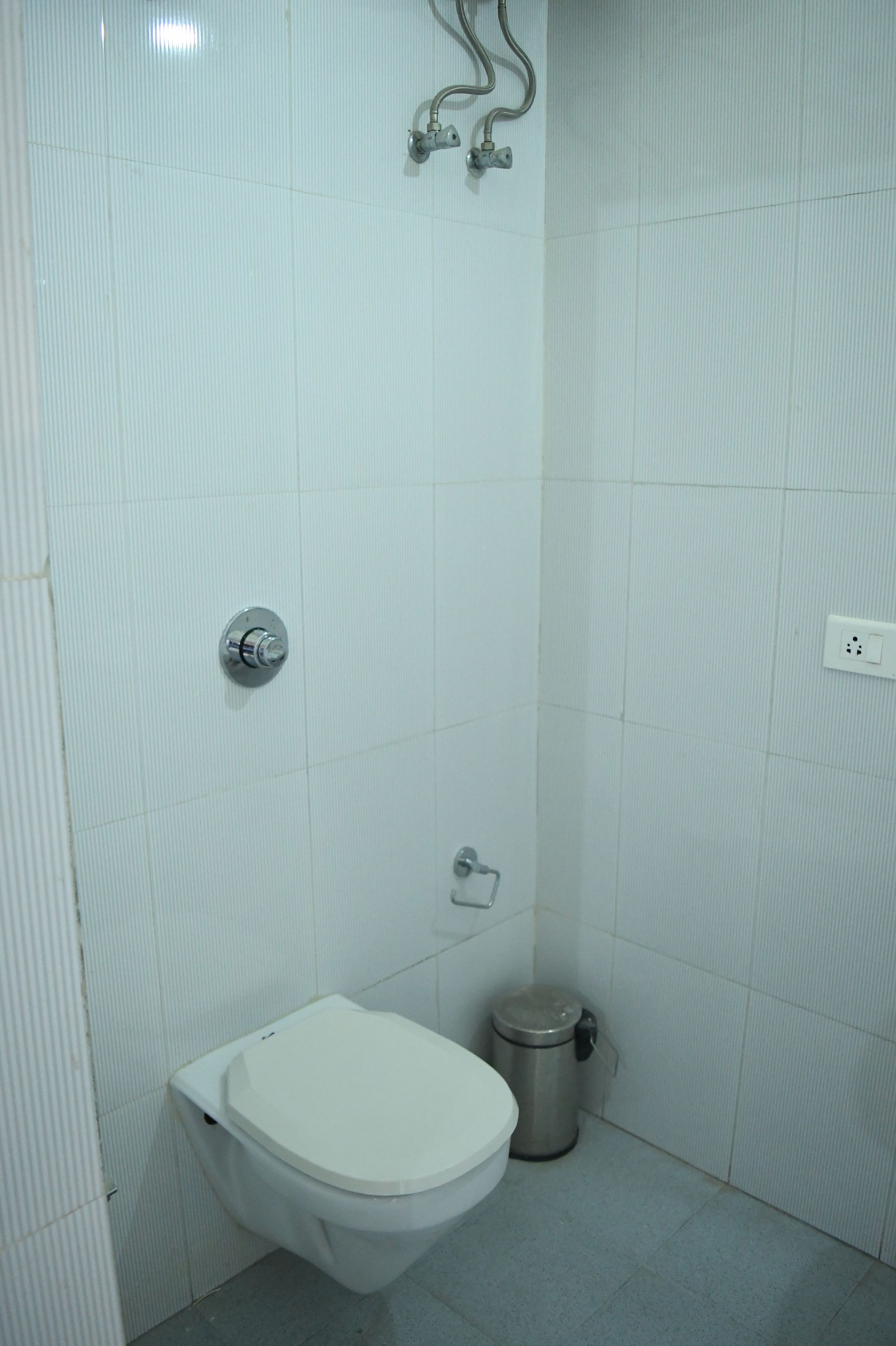Um banheiro pequeno com azulejos brancos, vaso sanitário, lixeira e chuveiro.