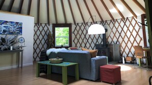 A cozy interior of a yurt with a sofa, a table, a lamp, and a window. - Totally secluded Yurt surrounded by waterfalls, brooks, cliffs and forest (Ulster Park)